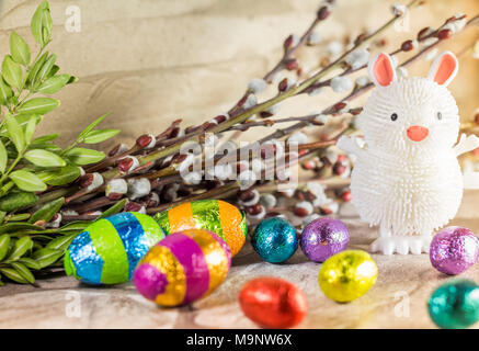 Easter decoration, toy rubber Bunny, chocolate eggs and shrub on rustic backdrop Stock Photo