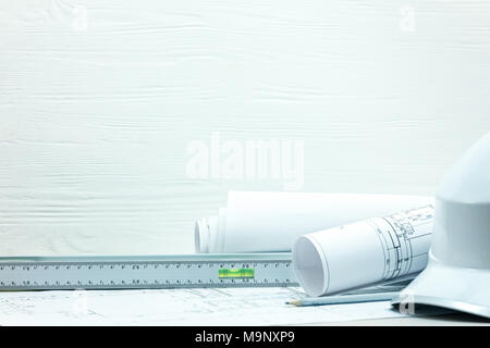 architects workplace desk. engineering tools, project drawings and blueprints, protective helmet against white wooden background. Stock Photo