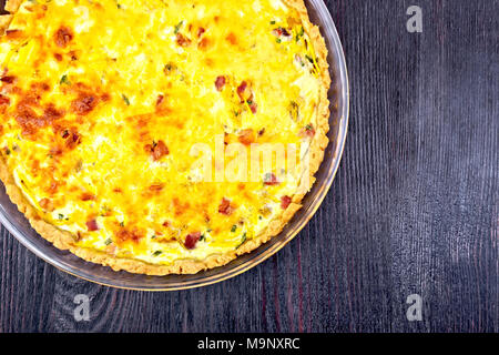 Pumpkin kish with pumpkin and bacon, filled with milk and eggs in a glass frying pan on the background of a wooden board from above Stock Photo