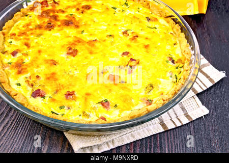 Pumpkin kish with pumpkin and bacon, filled with milk and eggs in a glass frying pan on a napkin, parsley, slices of a vegetable on a wooden plank bac Stock Photo