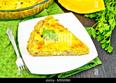 Piece of pie kish with pumpkin and bacon, filled with milk with eggs and cheese in a plate on a green napkin, parsley on a wooden plank background Stock Photo