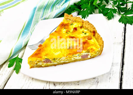 Piece of pie kish with pumpkin and bacon, filled with milk with eggs and cheese in a plate, parsley, napkin on a background of light wooden board Stock Photo