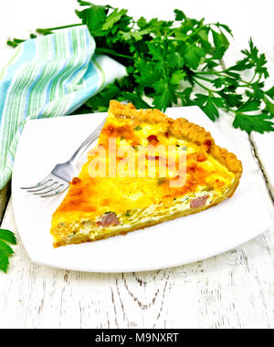 Piece of pie kish with pumpkin and bacon, filled with milk with eggs and cheese in a plate, parsley, towel on wooden plank background Stock Photo