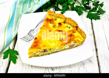 Piece of pie kish with pumpkin and bacon, filled with milk with eggs and cheese in a plate, parsley, napkin on a wooden board background Stock Photo