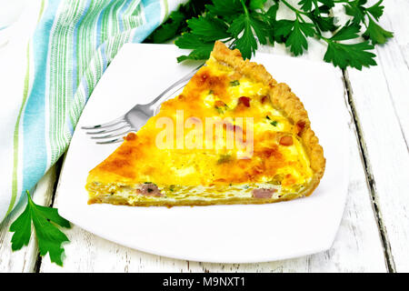 Piece of pie kish with pumpkin and bacon, filled with milk with eggs and cheese in a plate, parsley, towel on wooden plank background Stock Photo