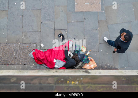 Looking down on a Homeless man sleeping with his dog outside a tube station whilst another man walks past. London, UK Stock Photo