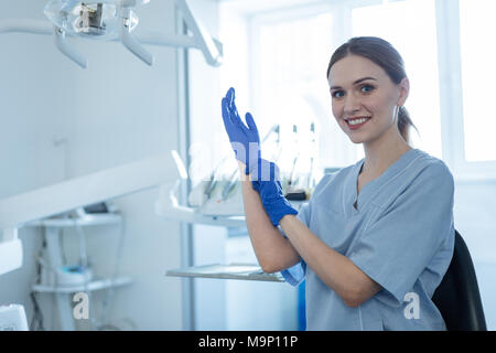 Upbeat female dentist putting on rubber gloves Stock Photo