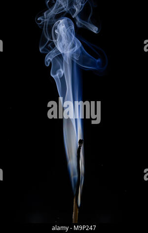 Burned match with blue smoke in front of a dark background, studio shot Stock Photo