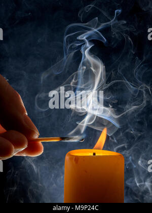 Lighting of a candle with smoking match in front of a black background, studio shot Stock Photo