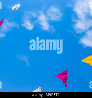 Multi-colored flags decoration hanging on a background of blue sky with white clouds. Copyspace Stock Photo