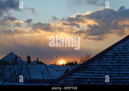 Dramatic sunset through gathering snow clouds over suburban rooftops Stock Photo