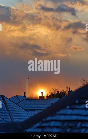 Dramatic sunset through gathering snow clouds over suburban rooftops Stock Photo