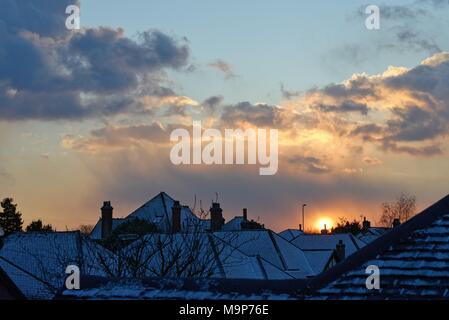 Dramatic sunset through gathering snow clouds over suburban rooftops Stock Photo