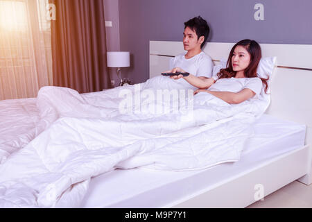 young couple lying on a bed with remote control and watching television in the bedroom Stock Photo