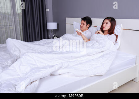 young couple lying on a bed with remote control of air conditioner in the bedroom Stock Photo