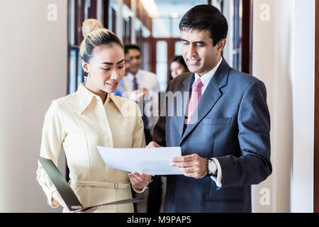 Executive and secretary standing in office hallway discussing papers Stock Photo