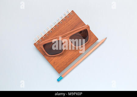 Wooden notepad, sunglasses and pencil on colorful background minimal creative flat lay concept. Stock Photo