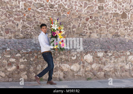 A Mexican man carries a flower arrangement to be used in creating an altar celebrating El Viernes de Dolores during Holy Week March 23, 2018 in San Miguel de Allende, Mexico. The event honors the sorrow of the Virgin Mary for the death of her son and is an annual tradition in central Mexico. Stock Photo