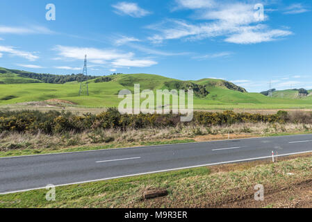 Road running alongside steel towers carrying power lines in a lush countryside in new zealand Stock Photo