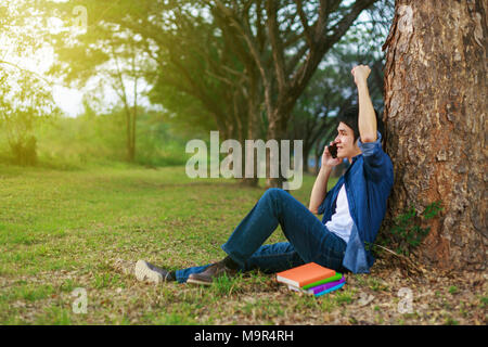 cheerful man talking on mobile phone with hand raised in the park Stock Photo