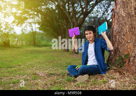 young man sitting and holding a book in the park Stock Photo