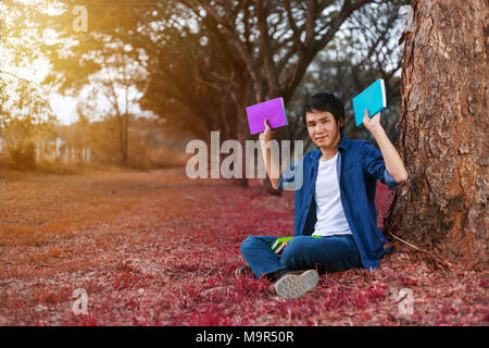 young man sitting and holding a book in the park Stock Photo