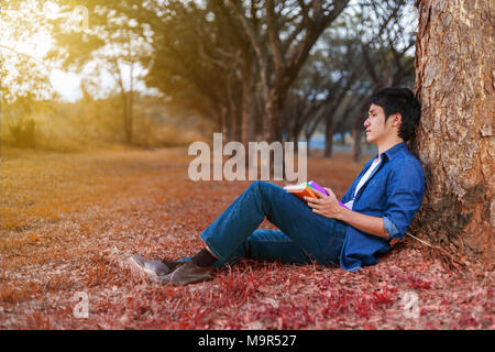 young man sitting and holding a book in the park Stock Photo