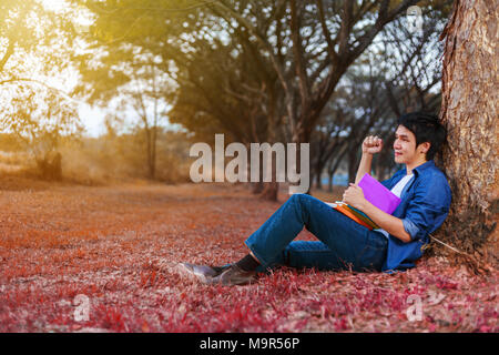 cheerful man  holding a book with arm raised in the park Stock Photo