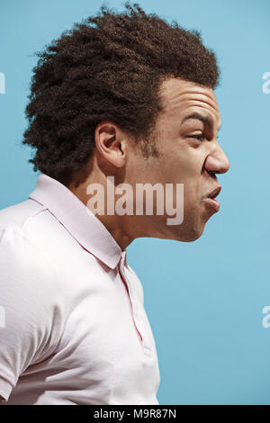 The young emotional angry man screaming on blue studio background Stock Photo