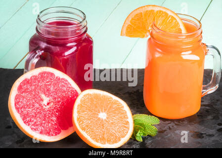 Freshly squeezed orange juice and grapefruit nectar, in mason jars, on a black stone plateau, with sliced orange and grapefruit and mint leaves near. Stock Photo