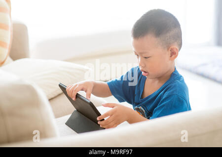 Young child addicted to technology gadget. Asian boy using digital tablet pc at home. Stock Photo