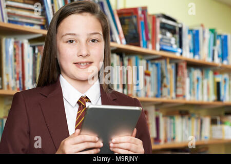 Portrait Of Girl Wearing School Uniform Using Digital Tablet In Library Stock Photo