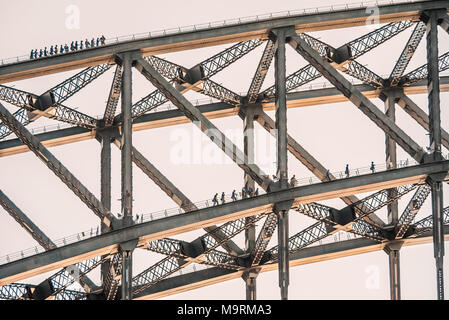 Tourists climb on two layers of the Sydney Harbour Bridge. The sun is catching the bottom of the metal bridge. Stock Photo