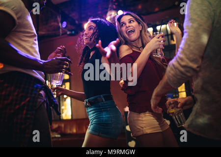 Happy young women dancing and partying with male friends at nightclub. Group of friends enjoying at bar with drinks. Stock Photo