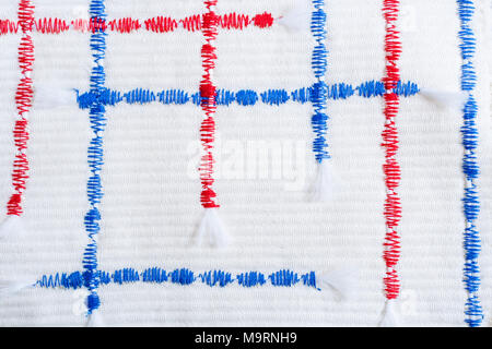 Vertical and horizontal red and blue textural zigzag seams on relief white fabric. Stock Photo