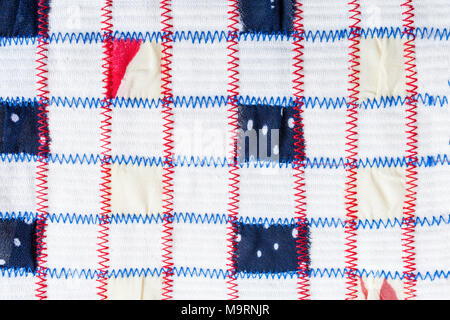 Textile pattern of square pieces of colored fabrics, sewn by red and blue zigzag seams on white fabric. Stock Photo