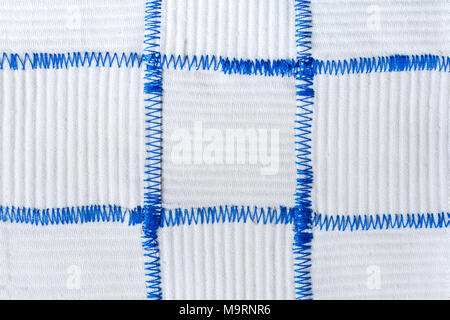 Hand-made textile background of square pieces of white fabrics sewn by blue zigzag seams.