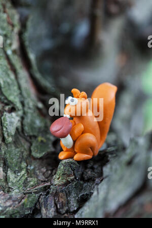 Plasticine world - small homemade squirrel holds in paws boletus mushroom and sitting on a tree , selective focus Stock Photo