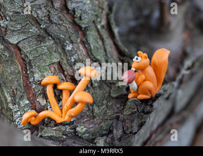 Plasticine world - small homemade squirrel holds in paws boletus mushroom and sitting on a tree , selective focus on head Stock Photo