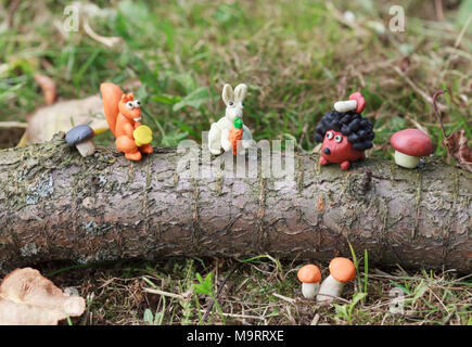 Plasticine world - little homemade squirrel with chanterelle, white bunny with a carrot and a hedgehog with mushroom sitting on a log, selective focus Stock Photo