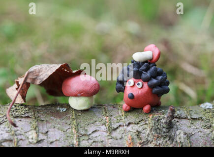 Plasticine world - small homemade hedgehog with boletus on his back sitting sitting next to a mushroom under a fallen autumn leaf, selective focus on  Stock Photo