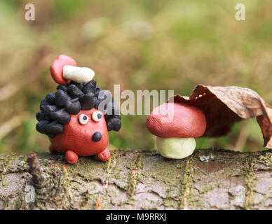 Plasticine world - small homemade hedgehog with boletus on his back sitting sitting next to a mushroom under a fallen autumn leaf, selective focus on  Stock Photo