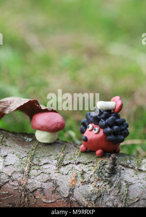 Plasticine world - small homemade hedgehog with boletus on his back sitting sitting next to a mushroom under a fallen autumn leaf, selective focus on  Stock Photo