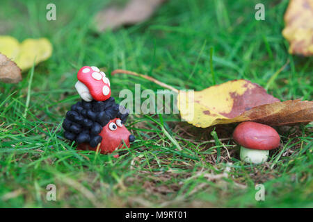 Plasticine world - small homemade hedgehog with fly agaric found boletus mushroom under a fallen autumn leaf, selective focus on the hedgehog Stock Photo