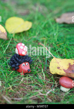 Plasticine world - small homemade hedgehog with fly agaric found boletus mushroom under a fallen autumn leaf, selective focus on the hedgehog Stock Photo