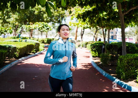 Happy girl jogging on the running track in the park Stock Photo