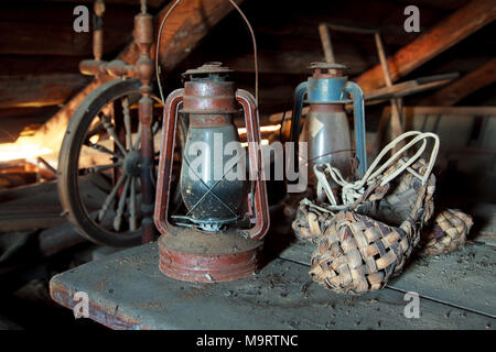 Russian vintage household items. Still life. Old spinning wheel, bast shoes and a kerosene lamp in a dusty garret in the country house. Selective focu Stock Photo