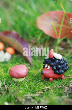 Plasticine world - small homemade hedgehog with boletus on his back on a green meadow surrounded plasticine mushrooms, selective focus on the hedgehog Stock Photo