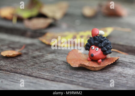 Plasticine world - small homemade hedgehog with boletus on his back surrounded by fallen autumn leaves, selective focus on the hedgehog Stock Photo