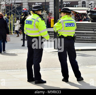 London, England, UK. Two female police officers in Piccadilly Circus - 'Up the Women' painted on the steps up to Eros Stock Photo